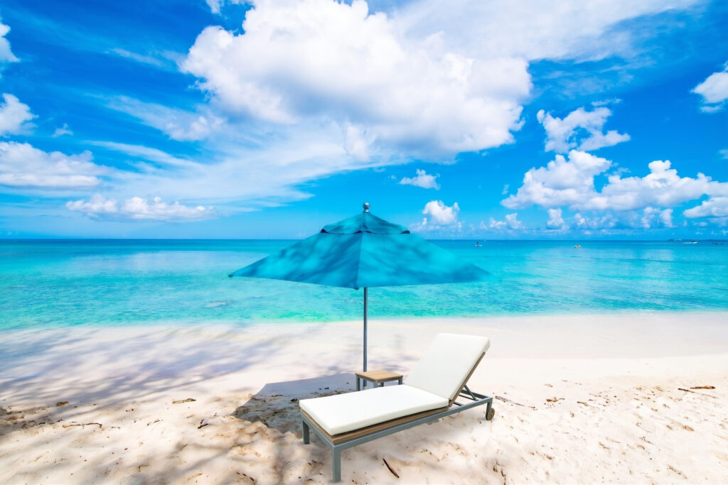 Celeste Resort teak sun lounger on a white sand beach with blue parasol and turquoise sea