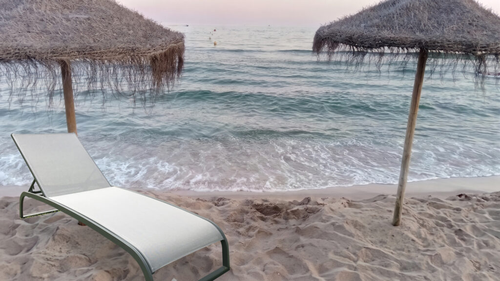 Riviera Prestige sculpted sun lounger on a white sand beach with blue parasol and turquoise sea