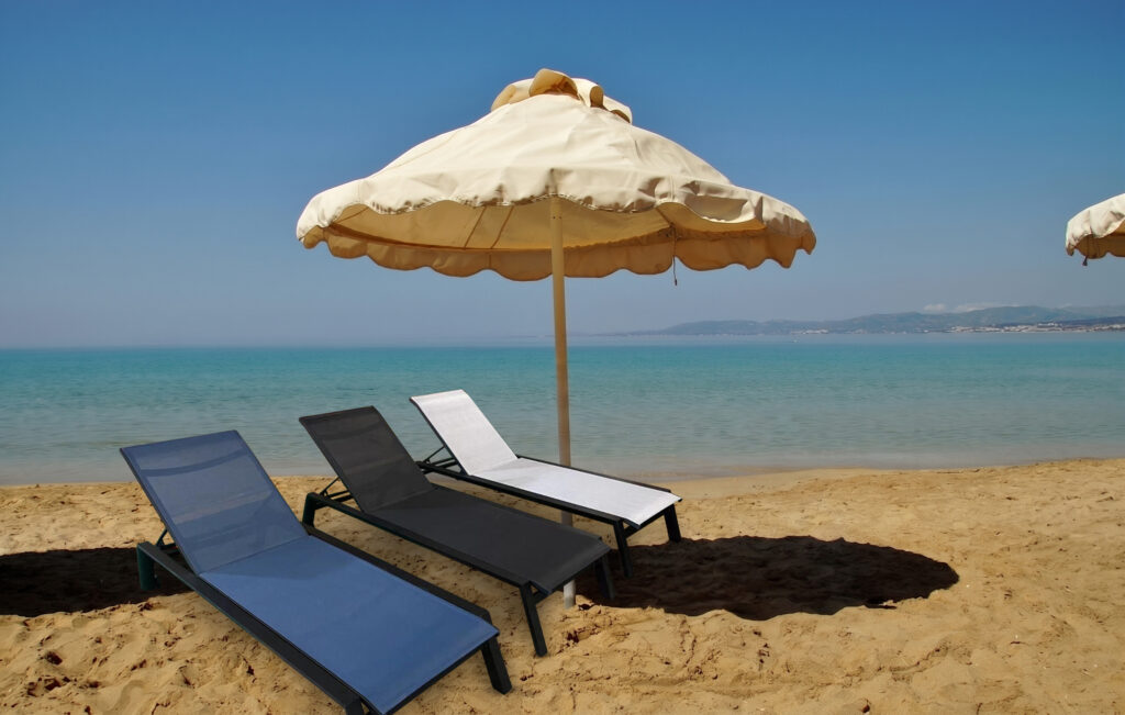 Valentina commercial sun lounger on a sandy beach with cream parasol and turquoise sea
