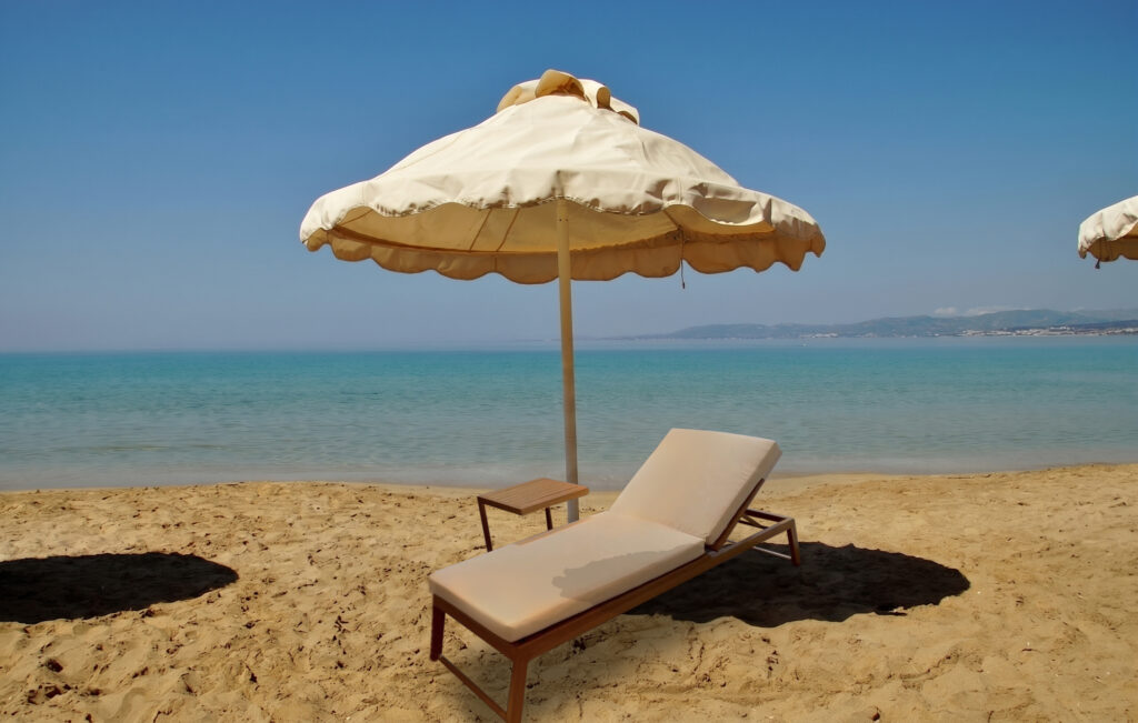 Verona Elite wood effect sun lounger on a sandy beach with parasol and sea view
